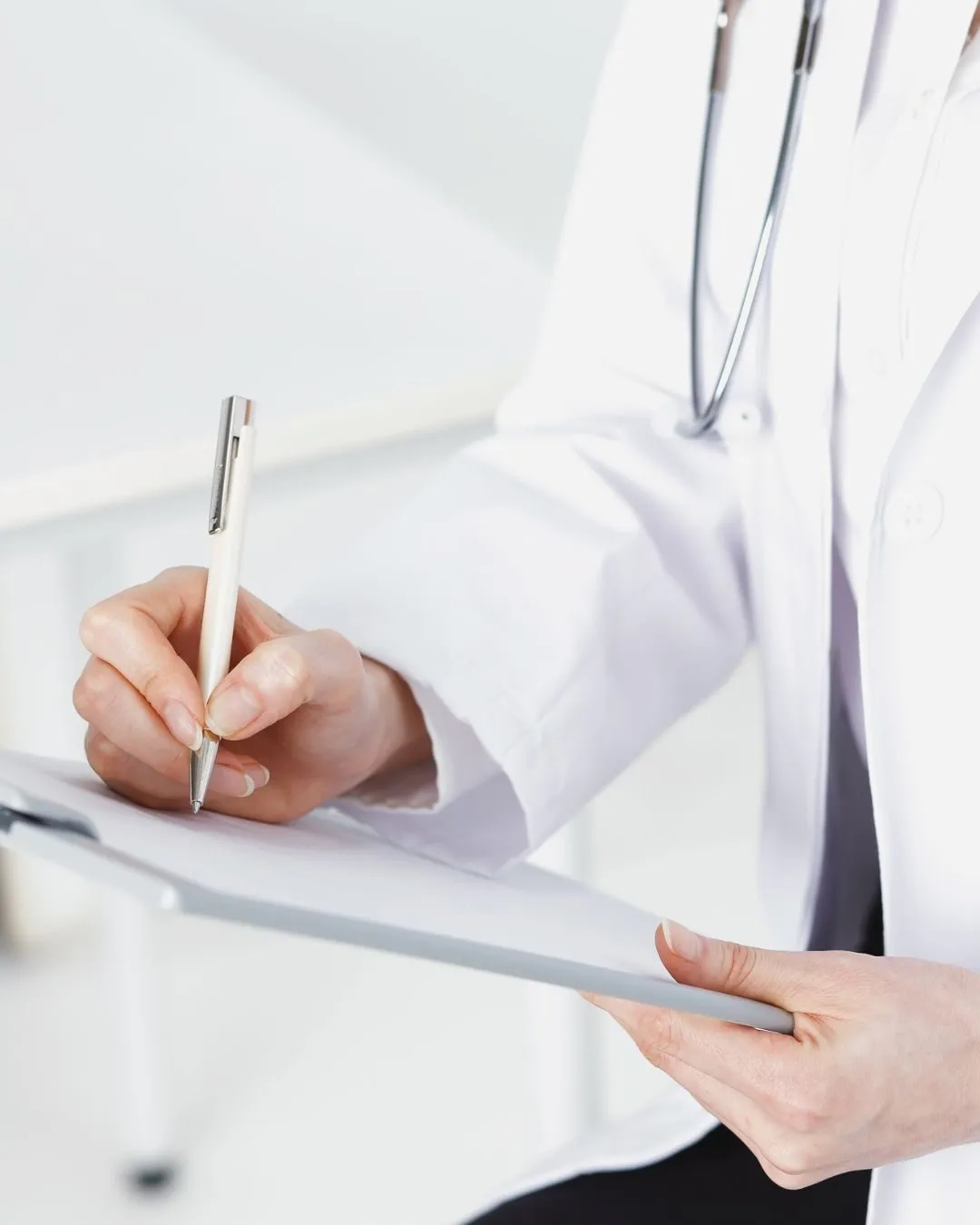 Clinician in a white coat writing notes on a clipboard